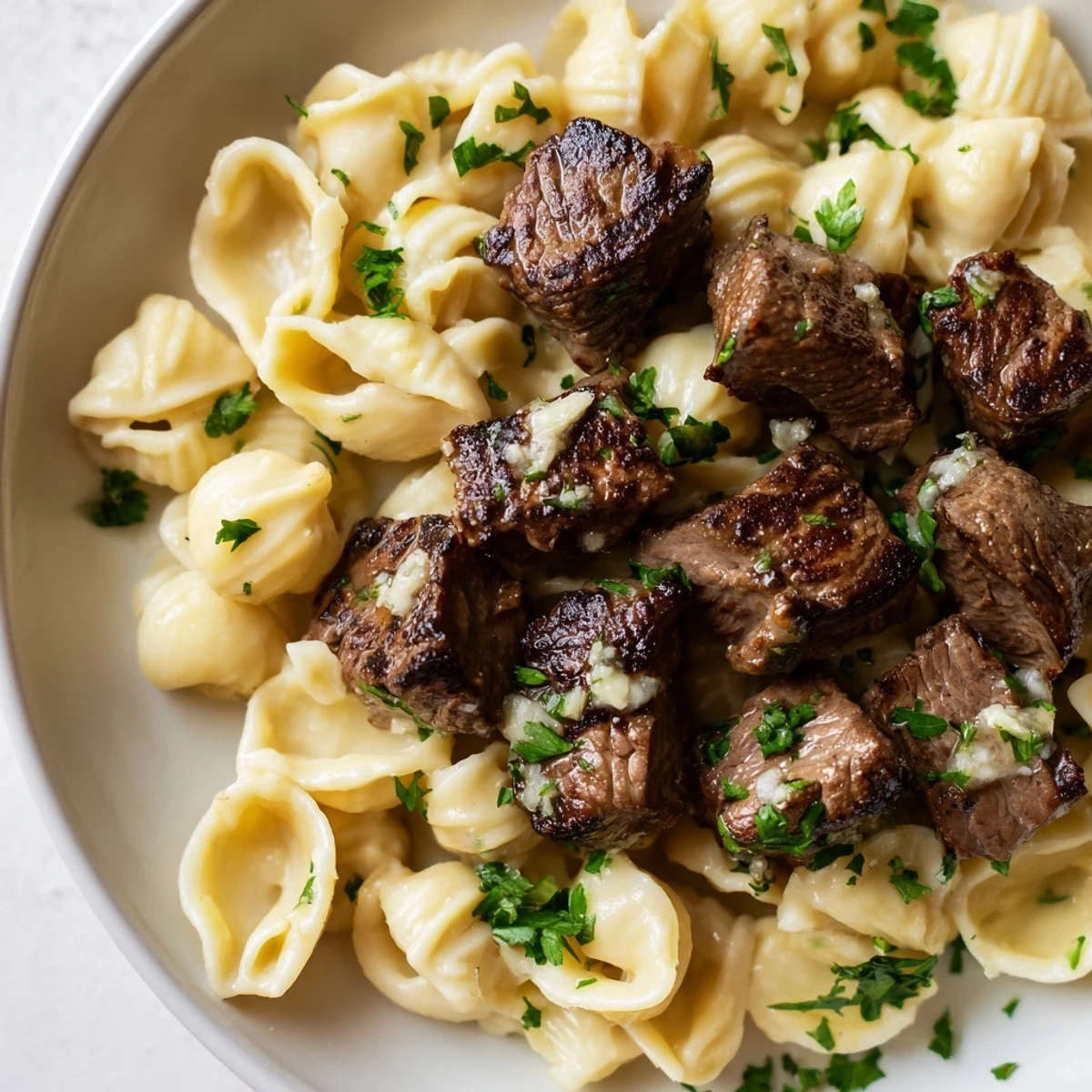 Sizzling garlic butter steak bites, fragrant with garlic, served atop creamy cheddar cheesy shells.