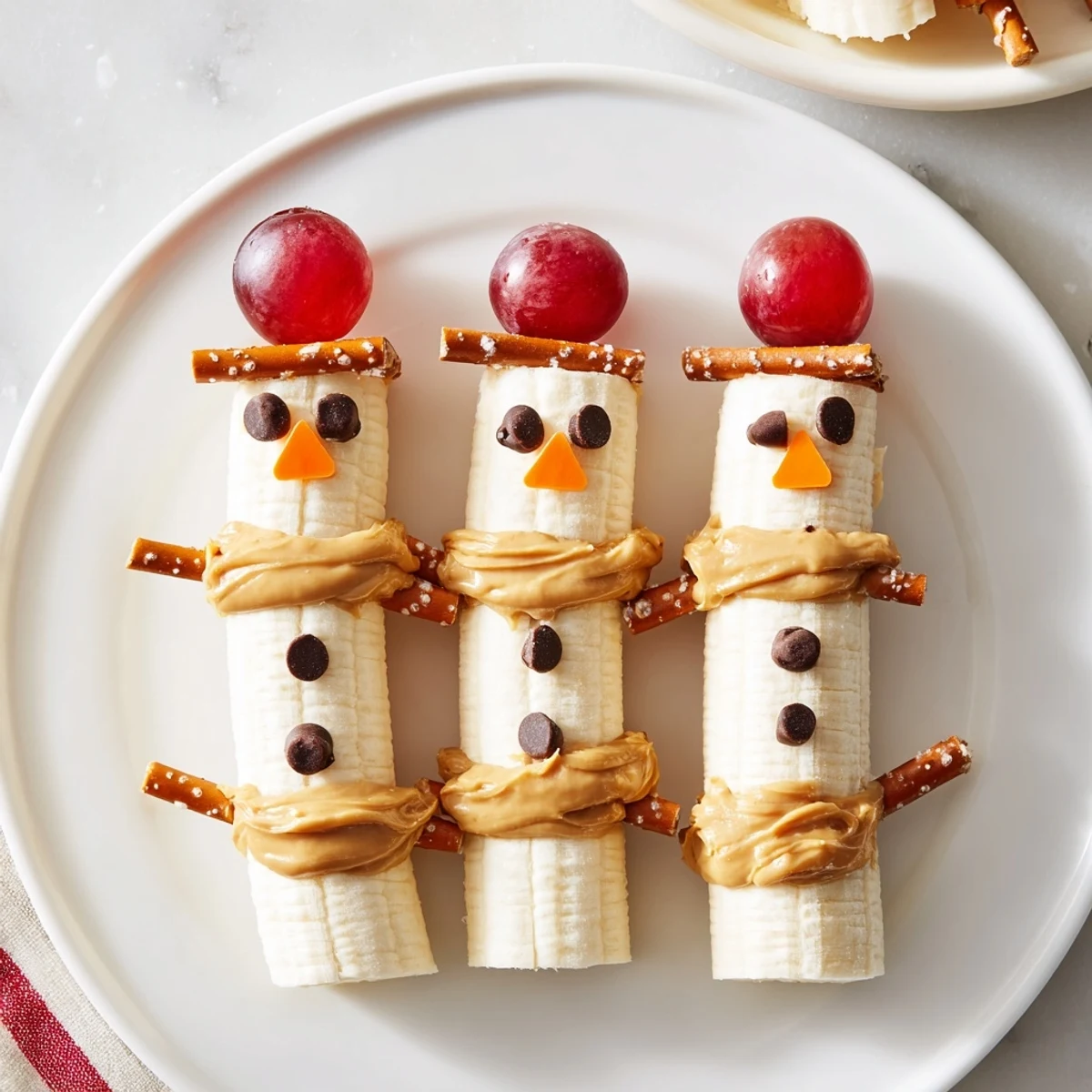 Adorable Banana Peanut Butter Snowmen are ready to eat, with chocolate chip eyes and pretzel arms.