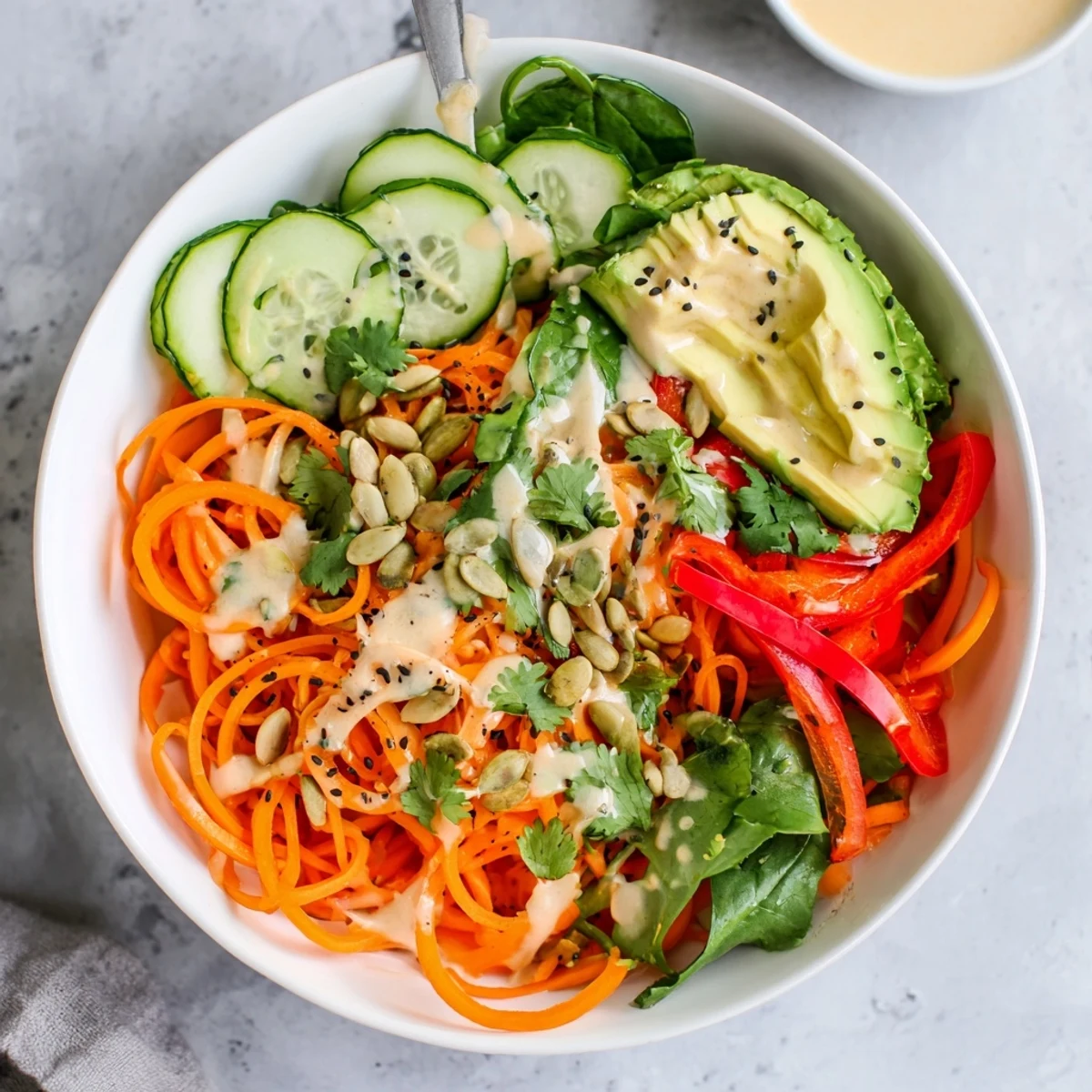 Bright overhead shot of a Carrot Noodle Skincare Bowl, showcasing colorful spiralized carrots, red bell pepper, cucumber, and toasted sesame seeds on a rustic wooden table.