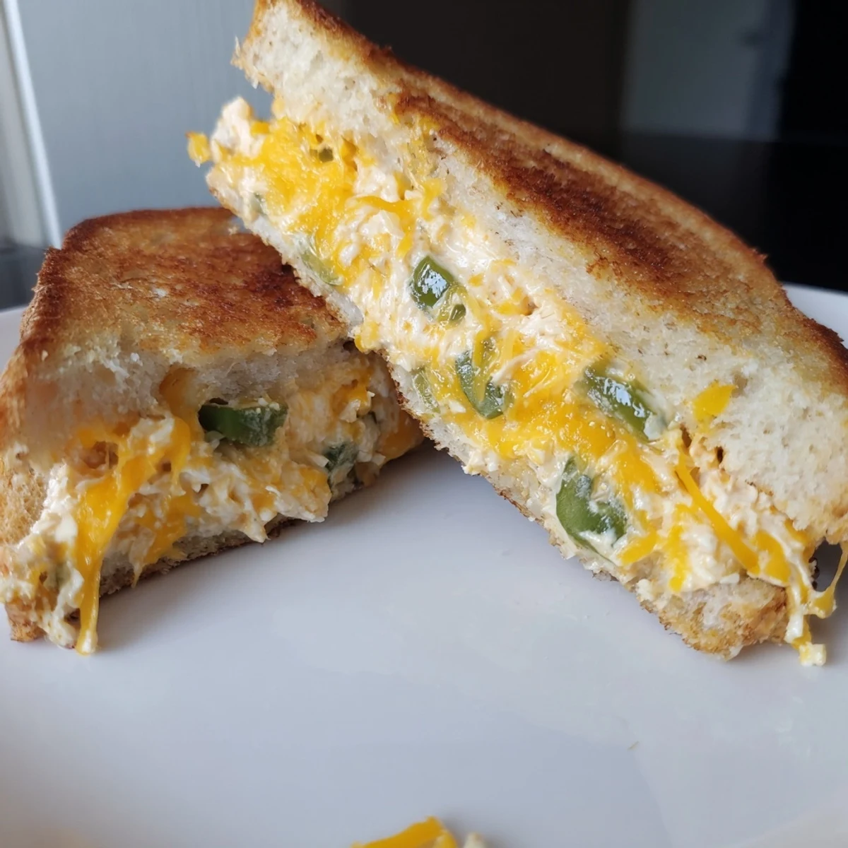 Close-up of jalapeño popper grilled cheese with crisp crust, showcasing creamy filling and vibrant chopped jalapeño bits.