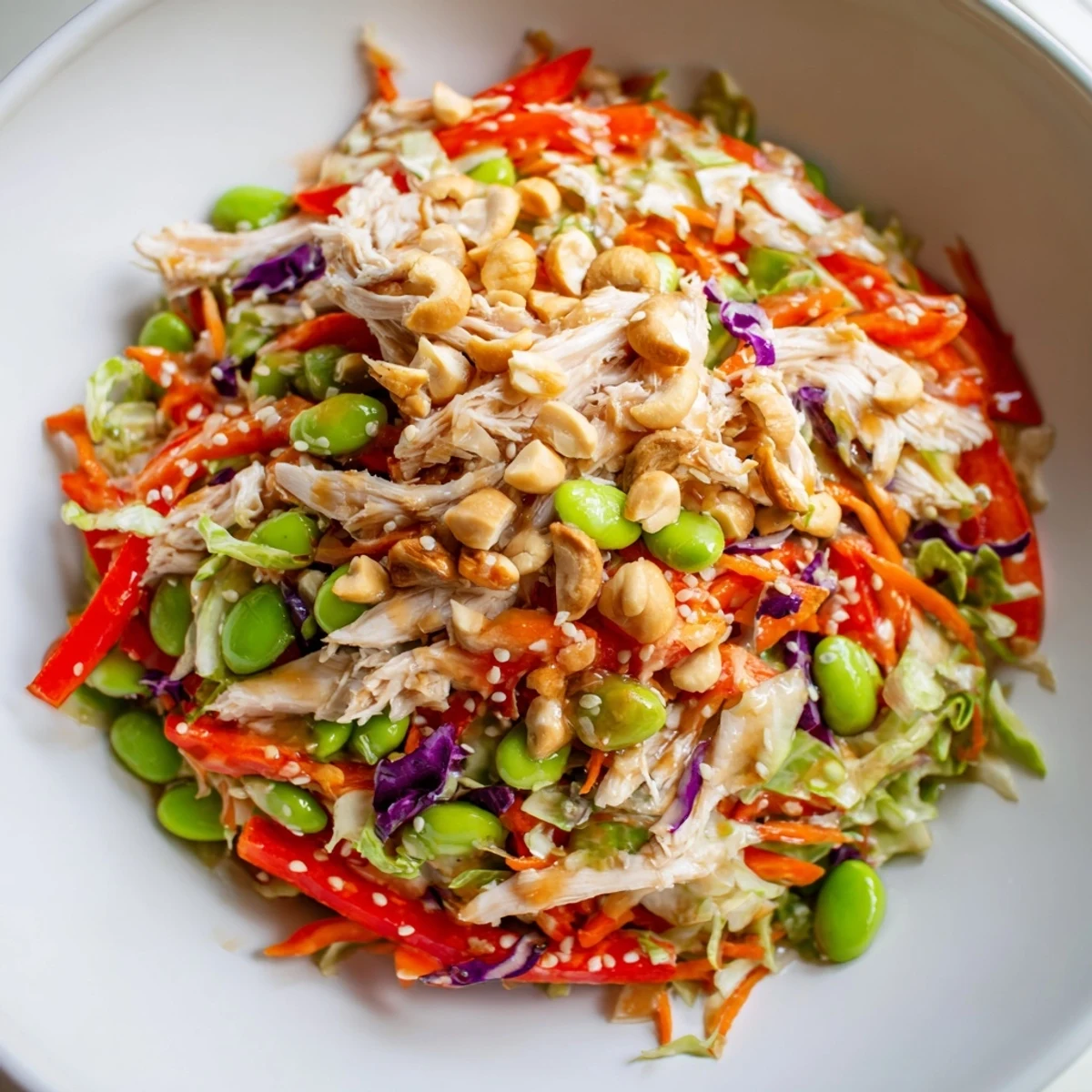 A vibrant, protein-packed Edamame Crunch Chicken Salad garnished with green onions and red bell pepper, served on a light wooden table.