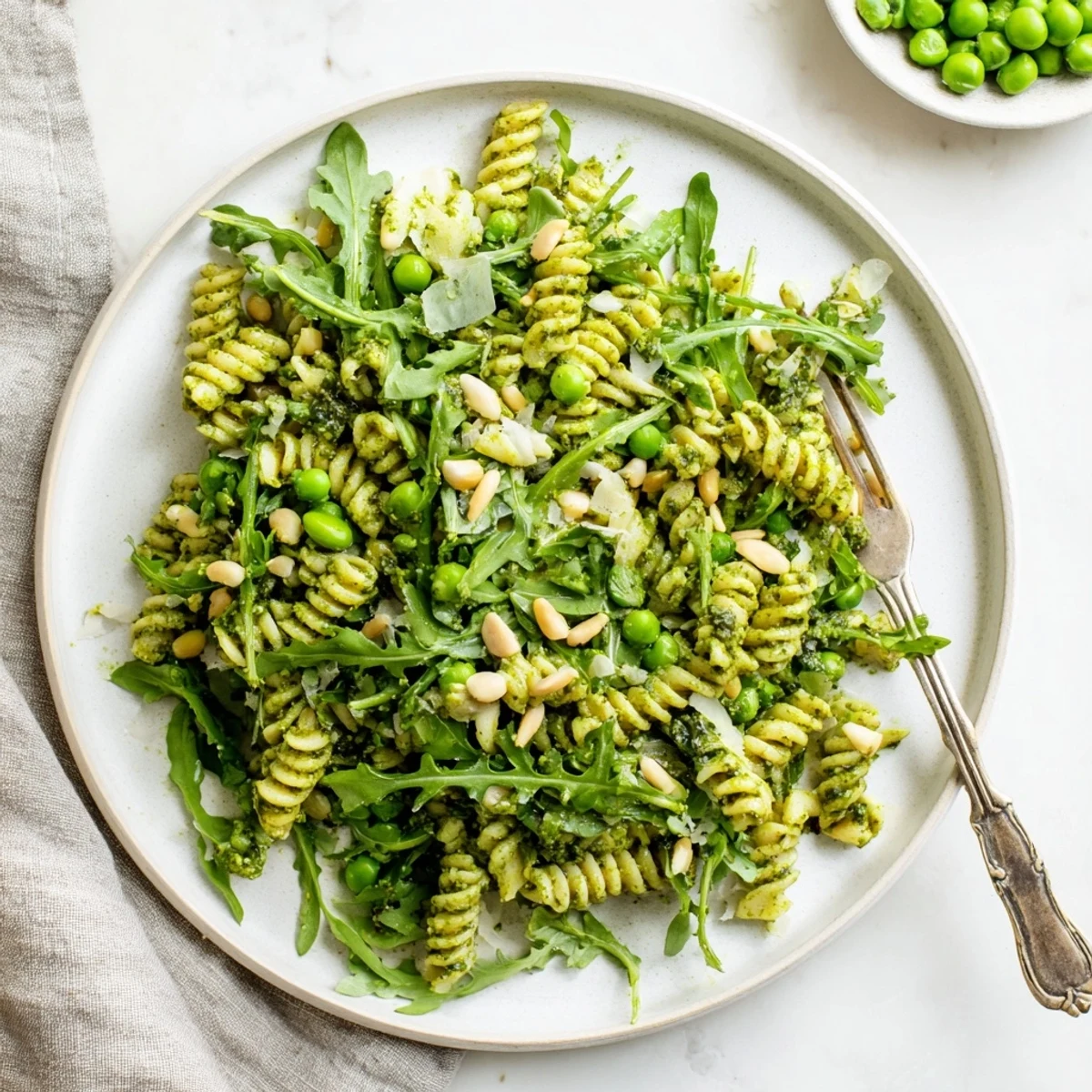 Spring Green Pesto Pasta Salad shown in a chilled bowl with vibrant green pesto coating fusilli, sweet peas, peppery arugula, and toasted pine nuts.
