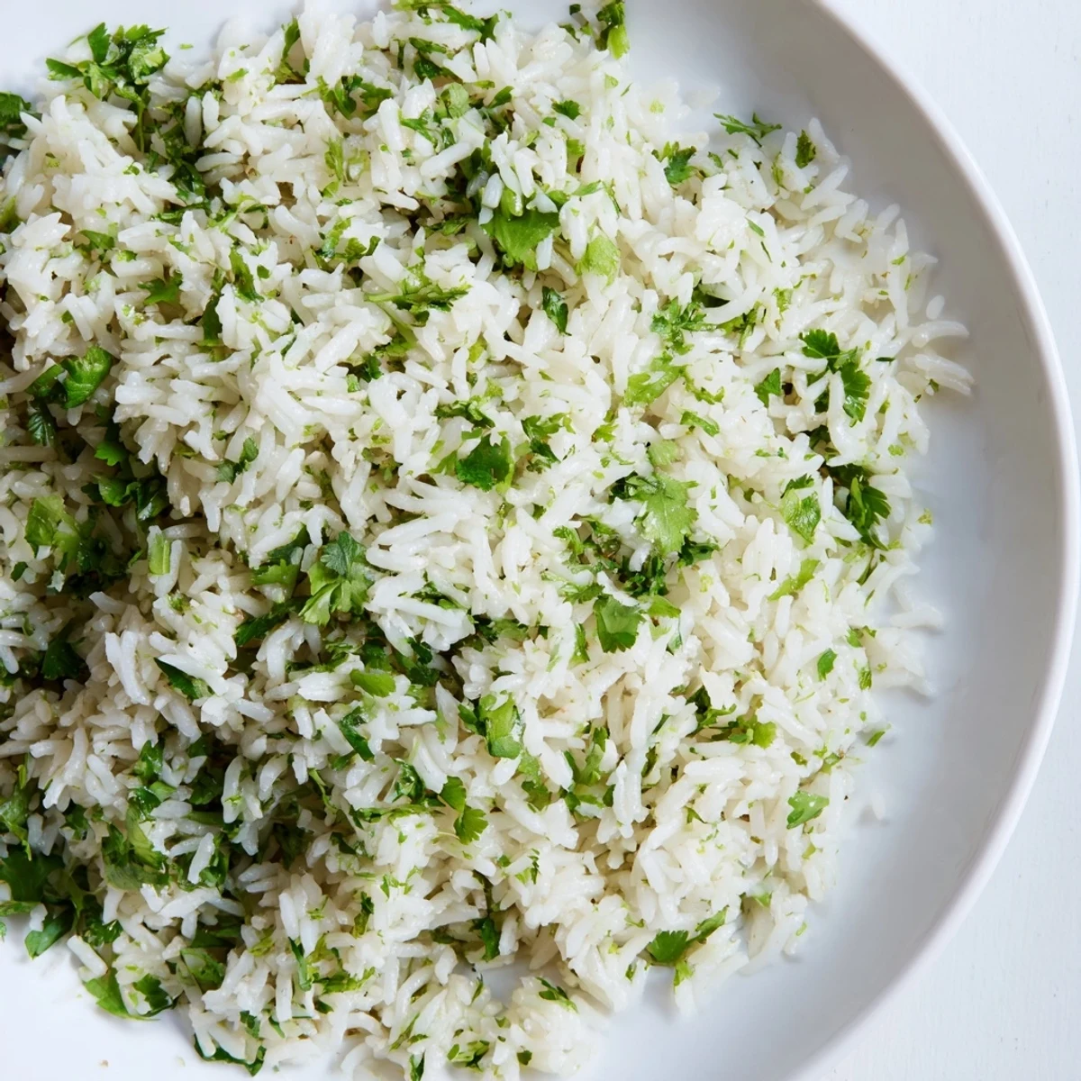 A close-up of fluffy Cilantro Lime Rice garnished with fresh green cilantro leaves and vibrant lime zest, steaming in a white bowl.  