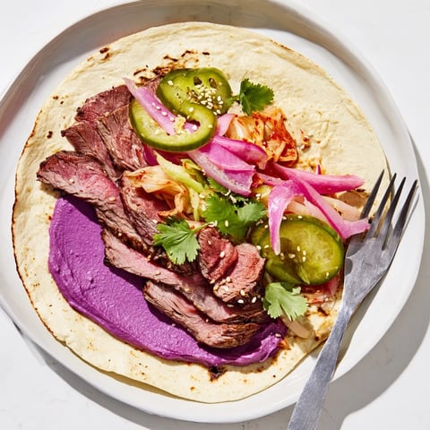 Colorful Global Street-Food Fusion Tacos filled with spicy beef, fresh veggies, and ube crema.