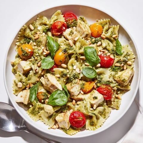 Creamy pesto chicken bowtie pasta garnished with fresh basil and pine nuts.