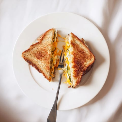 Melted cheese spills from this gooey pickle grilled cheese sandwich, a perfect comfort food.