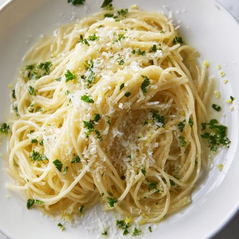 Steaming capellini noodles tossed in a glossy lemon butter sauce, garnished with fresh parsley and Parmesan, served in a white pasta bowl.  