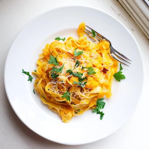 Freshly roasted butternut squash cubes and golden garlic cloves rest on a parchment-lined baking sheet, ready to be blended into a creamy pasta sauce.
