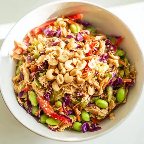 Close-up of Edamame Crunch Chicken Salad in a white bowl, topped with toasted sesame seeds and roasted cashews for added texture and crunch.