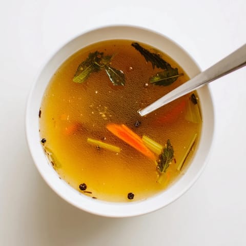 Golden Vegetable Broth From Scraps simmering in a stockpot with peppercorns and bay leaves for rich flavor.  