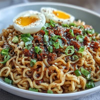 A steaming bowl of viral garlic butter ramen with glossy noodles coated in rich, savory sauce and topped with sliced green onions and a soft-boiled egg.